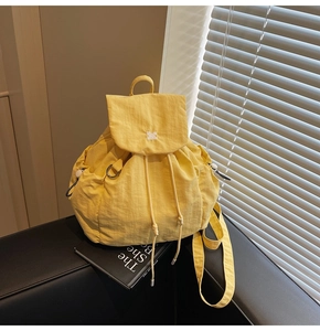 Dettaglio di uno zaino in nylon giallo con chiusura a patta e dettagli ricamati bianchi