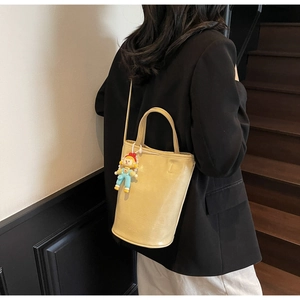 Fashionable cream bucket bag with clown charm worn over a classic black blazer
