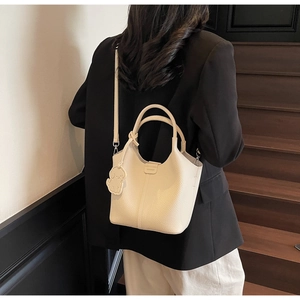 Detail of off-white lychee grain leather bucket bag with cute dog charm on wood stairs