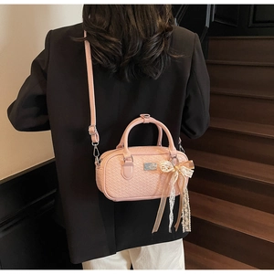 Borsa Boston rosa intrecciata con ciondolo a fiocco di perle portata su un blazer nero