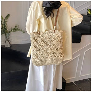 Detail of hand-woven straw tote bag with wavy patterns and brown shoulder strap