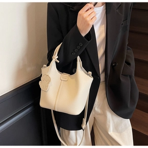 Detail of off-white lychee pattern bucket bag with cute dog charm and dual straps