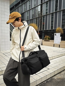 Grand sac de voyage en nylon noir avec plusieurs poches présenté dans un décor urbain moderne