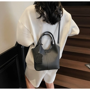 Black lychee texture leather bucket bag with dog charm on a wooden staircase