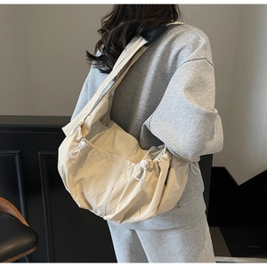 Side view of beige canvas crossbody bag featuring adjustable strap and drawstring detail