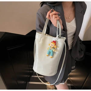 Detail view of cream bucket bag with glossy finish and cute cartoon doll pendant