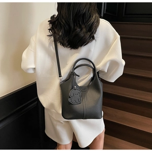 Detail view of black pebble leather bucket bag with cute dog charm on a white outfit