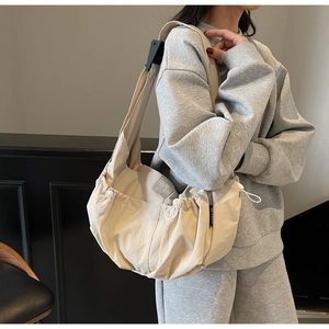 Detail of beige dumpling bag with drawstring folds and wide black adjustable shoulder strap