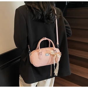 Dettaglio della borsa Boston rosa intrecciata con ciondolo a fiocco e placca logo dorata