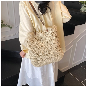 Detail of hand-woven straw bucket bag featuring scalloped edges and brown leather straps