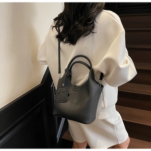 Detail of black lychee grain bucket bag with dual handles and dog charm on stairs