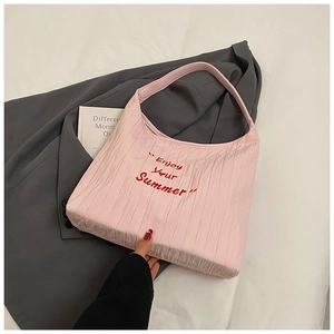 Détail du sac demi-lune rose plissé avec broderie posé sur une veste de costume