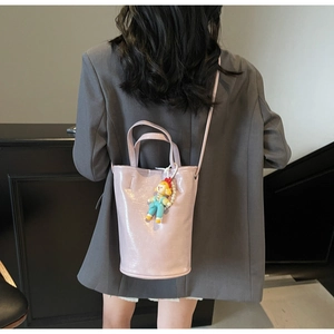 Detail of light pink bucket bag with smooth texture and cartoon doll pendant accessory