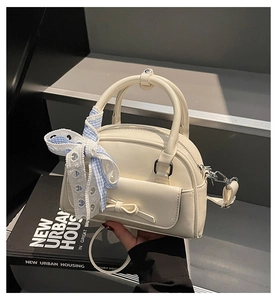 Detail of cream-colored crossbody bag with bow decoration and blue checkered ribbon strap