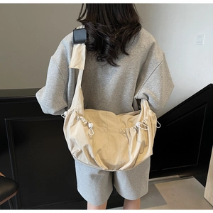 Detail view of beige dumpling crossbody bag featuring adjustable white drawstrings