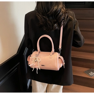 Modello con borsa Boston rosa lucida, ciondolo a fiocco di perle e logo argento