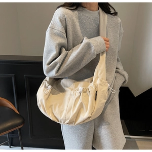 Close-up of beige dumpling bag featuring side drawstring pleats and wide shoulder strap
