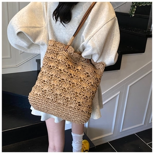 Detail of woven straw tote bag featuring brown PU leather strap and hollow wave texture