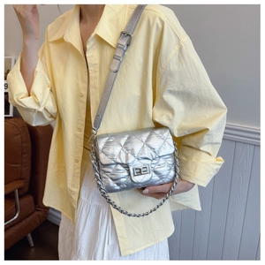Silver quilted crossbody bag with metal chain strap worn by model in a stylish home setting