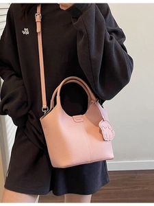Pink lychee grain leather bucket bag with dog charm shown on shoulder