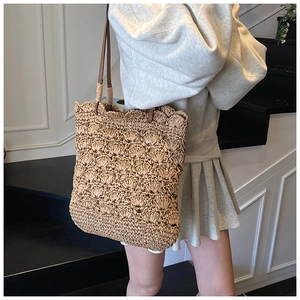 Detailed view of hand-woven straw beach tote with premium brown leather shoulder straps
