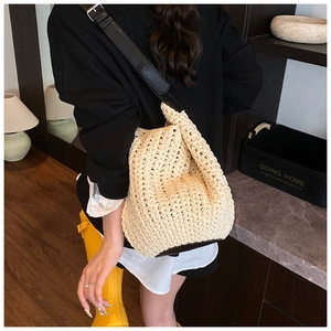 Detail of woven straw bucket bag with black leather trim and adjustable shoulder strap