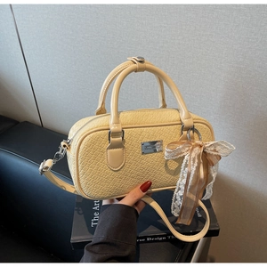Dettaglio borsa Boston beige in pelle con trama a coccodrillo e ciondolo con fiocco