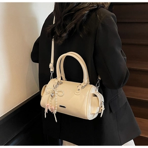 Dettaglio della borsa Boston bianco crema con finitura lucida e ciondolo a fiocco di perle