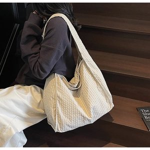 Close-up of a cream grid canvas tote bag with wide strap on wooden stairs