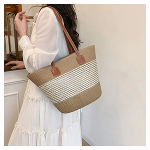 Dettaglio borsa tote in paglia intrecciata con manici in pelle marrone su abito bianco