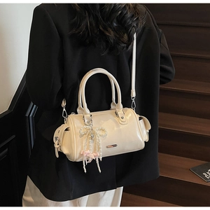 Close-up of off-white Boston bag with pearl bow charm and utility side pockets worn by model