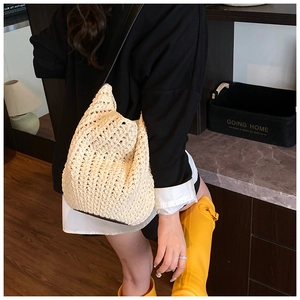 Detail of a beige woven bucket bag showing natural texture and crossbody style on a model