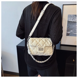 Detail of creamy white quilted shoulder bag featuring a metallic swivel lock and chain strap