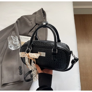 Dettaglio borsa nera con trama intrecciata, logo in metallo e ciondolo a fiocco