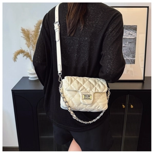 Close-up of quilted cream crossbody bag with silver chain strap and metal swivel lock