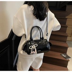Detail of glossy black patent leather Boston bag featuring a pearl bow charm on stairs