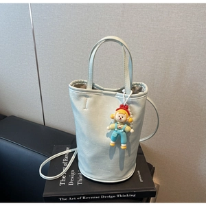 Detail of light blue bucket bag with fashion logo, clown charm, and long shoulder strap