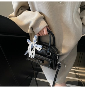 Detail of black crossbody bag featuring a bow pocket and checkered scarf on the handle