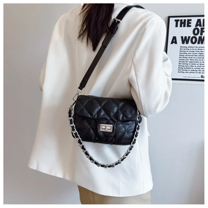 Detail shot of a black quilted shoulder bag with silver clasp and metal chain strap