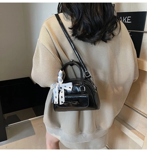 Detail of black patent leather handbag with decorative silk scarf on handle and bow accent