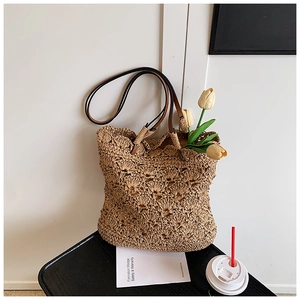 Detail of hand-woven straw tote bag with intricate floral patterns and leather straps
