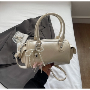 Dettaglio borsa Boston crema con fiocco di perle, ciondolo a cuore e nastro di seta