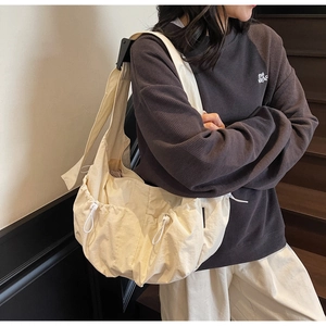 Detailed side view of beige dumpling crossbody bag with drawstring pocket on a model