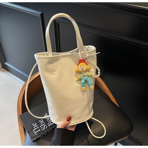 Detail of white bucket bag with pearl chain, cartoon charm, and faux leather texture