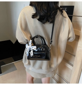 Detail of black glossy leather handbag with bow and ribbon handle held by model