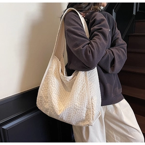 Detail of a beige quilted oversized tote bag showing textured fabric and shoulder strap