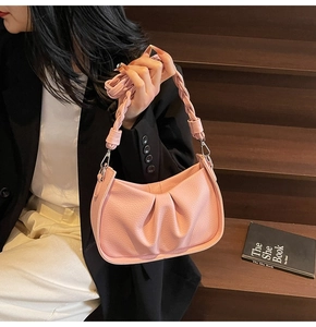 Detail view of pink pleated leather shoulder bag with a woven handle on wooden stairs