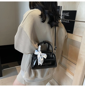 Detail of black patent leather mini bag with bow decoration and checkered silk ribbon