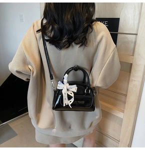 Detail of black patent leather Boston bag with bow and striped scarf on handle