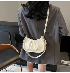 Detail of white pleated cloud bag with braided handle and slim strap worn with a grey blazer